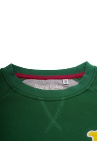 Grön sweatshirt med rund halsringning, med röda detaljer och en gul design. Texturerad tyg med synliga sömnadsdetaljer.