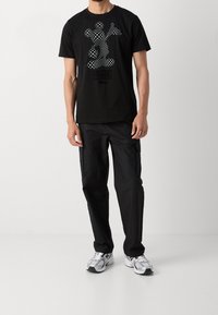 Černé bavlněné tričko s monochromatickým grafickým designem Mickey Mouse. V kombinaci s černými cargo kalhotami a šedými teniskami s černými akcenty.