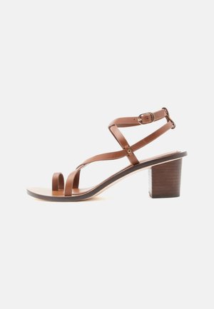 Sandale à talon en cuir marron avec boucle pour l'orteil, bride réglable à la cheville et talon bloc, vue de côté sur fond blanc.