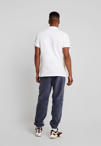 Vit polo-shirt, gråa joggers och mönstrade sneakers. Synlig krage, korta ärmar, uppvikta jogger-ändar och sportig skodesign.