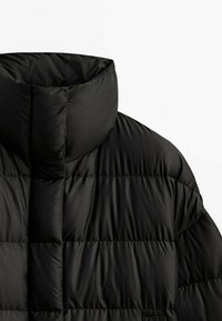 Giubbotto imbottito nero con colletto alto, caratterizzato da sezioni trapuntate, texture liscia e design minimalista. Nessun hardware o accenti visibili.