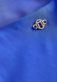 Blauwe stof met zowel gladde als gestructureerde delen, met een gouden ronde sluiting die duidelijk is bevestigd.