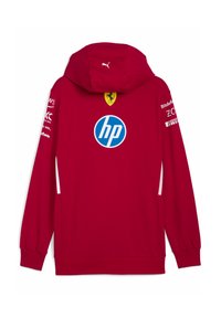 Sarkana kapucēta džemperis ar priekšējo logo, kurā ir baltas akcenti uz piedurknēm un sāniem. Aizmugurē atrodas Ferrari logo un Puma zīmola nosaukums.