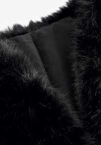 Gros plan d'un vêtement noir avec bordure en fourrure douce et dense et doublure en tissu lisse, mettant en valeur la texture et le contraste entre les matériaux.