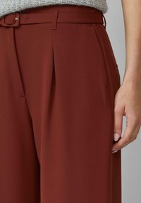 Roodbruine wijde broek gemaakt van soepel materiaal, met voorplooien en een bijpassende riem. Voorzien van zijzakken.