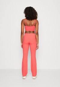 Korallenfarbener, gerippter Stoff, tailliertes Bralette und weit geschnittene Hose. Minimalistisches Design mit dünnen Trägern und nahtlosem Bündchen. Glatte Textur.