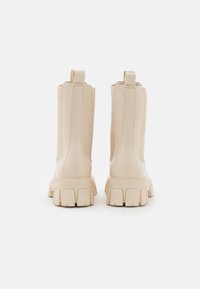 Bottes à talons carrés en cuir beige clair, avec une tige texturée, des coutures apparentes et une semelle épaisse à rainures.