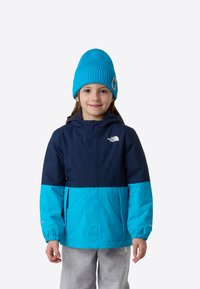 Jachetă cu blocuri de culoare albastru și bleumarin, cu glugă și manșete elastice, având logo-ul North Face pe piept, asortată cu o căciulă albastru deschis.