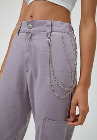 Pantalons lilas en tissu texturé, avec un accent de chaîne argentée sur le côté, une fermeture à bouton et des poches latérales.