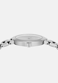 Hõbedane metallist käekell õhukese ümarate nägudega, lingitud rihm ja kroon, millel on graveering "A|X" lihtsal taustal.