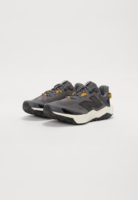 Chaussures de sport grises avec une tige en mesh, semelle extérieure en caoutchouc noir et accents jaunes. Remarquables par leur conception légère et leur forme distinctive.