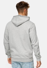 Grå sweatshirt med hætte, præget af sort tekst på indersiden af kraven, designet med en afslappet pasform og ribbede manchetter og kant.