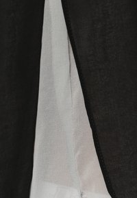 Indumento bianco e nero che mostra uno strato esterno nero texture e uno strato interno bianco liscio. Presenta cuciture visibili lungo i bordi.