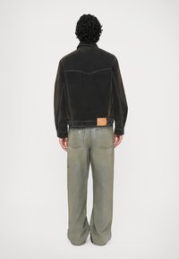 Giacca di denim nera con un design strutturato, con un'etichetta sulla vita posteriore. Pantaloni larghi di un verde sbiadito con due tasche posteriori.