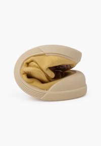 Scarpa di tela gialla, piegata con una suola in gomma texturizzata e una punta rinforzata. L'interno presenta una fodera liscia con cuciture visibili.