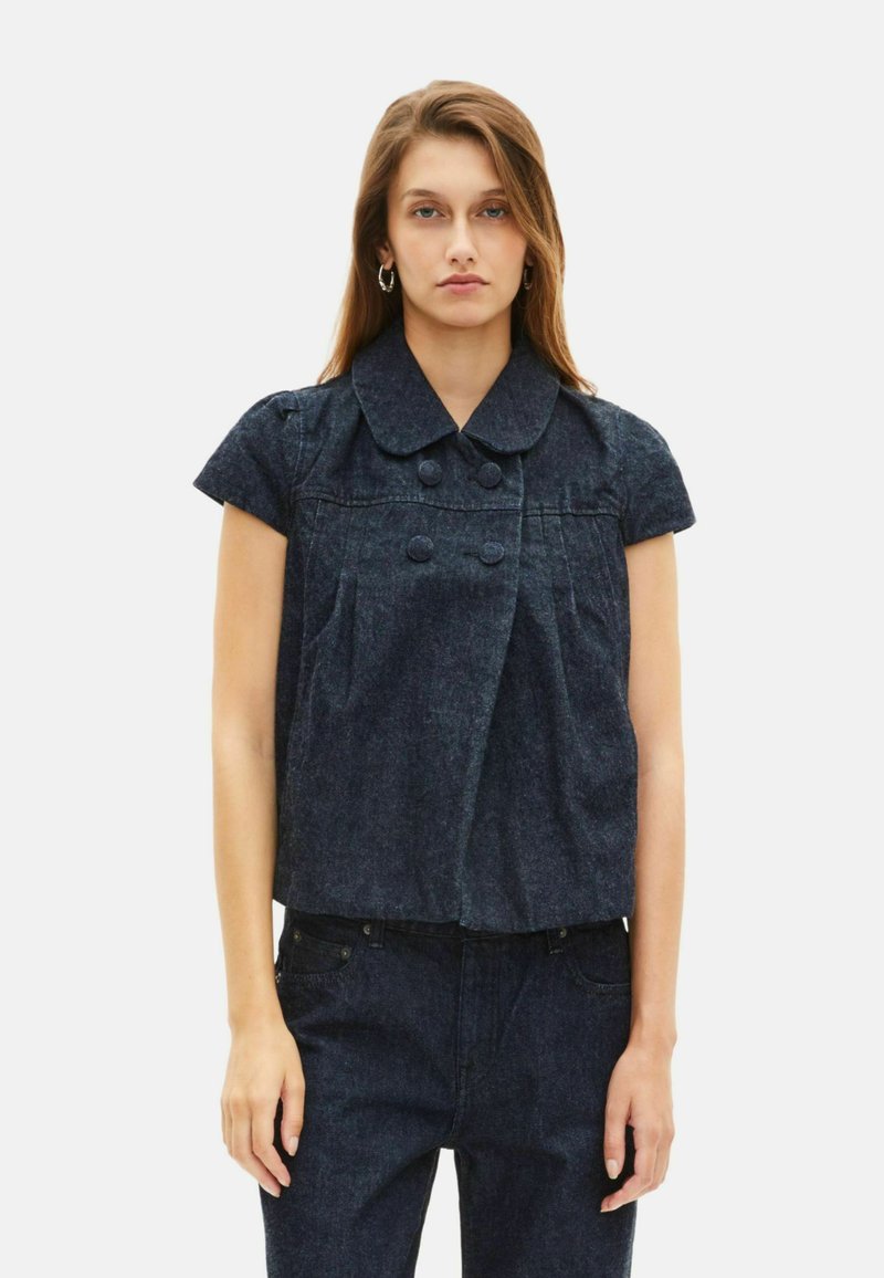 Giacca cropped in denim scuro con ampio colletto, maniche corte, doppi bottoni e tasche frontali. Design essenziale e tessuto testurizzato.