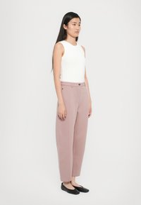 Haut sans manches blanc associé à un pantalon taille haute rose clair, ajusté, et des chaussures plates noires. Tissu lisse, coupe droite, détails minimaux.