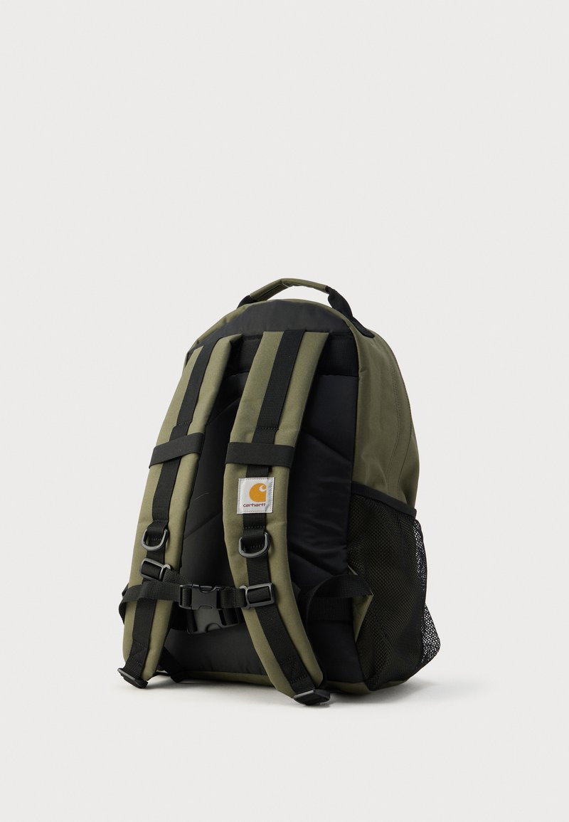 Rucksack aus olivgrünem Stoff, schwarze Akzente, gepolsterte Träger, verstellbare Schnallen und Netzseitentasche. Logo-Patch auf der Vorderseite.