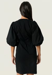 Schwarzes Kleid mit taillierter Silhouette, puffärmel und einem Reißverschluss auf der Rückseite. Glatter Stoff in einfarbiger Ausführung und mittlerer Oberschenkel Länge.