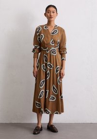 Braunes Midikleid mit Wickeldesign, das schwarz-weiße Blättermuster aufweist. Lange Ärmel mit Manschetten und taillierten Gürtel. Glatte Textur.