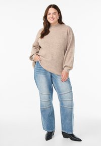 Beige Rippstrickpullover mit hohem Kragen, kombiniert mit hellblauen Jeans mit horizontalen Nähten und schwarzen Absatzstiefeletten.