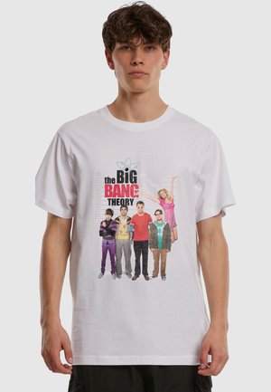 Νεαρός άνδρας με λευκό T-shirt που έχει τυπωμένο το καστ της σειράς The Big Bang Theory και τον τίτλο της εκπομπής μπροστά.