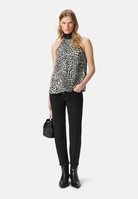 Halternektop in het wit met zwart luipaardprint, gedragen met slim fit zwarte broeken en zwarte enkellaarsjes. Inclusief een kleine zwarte handtas.