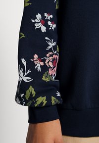 Navy sweater with floral print on the sleeve featuring pink, white, and green flowers; ribbed cuff and hem with a soft texture.