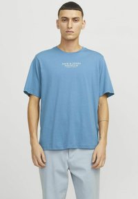 Gaiši zils īsām piedurknēm krekliņš no kokvilnas, ar baltu „JACK & JONES PREMIUM” logo krūtīs. Vienkārša, brīva piegriezuma dizains.