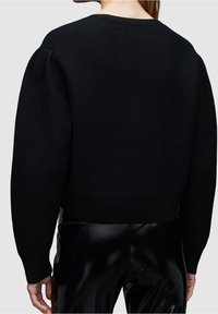 Schwarzer, verkürzter Pullover aus strukturiertem Stoff, mit Rundhalsausschnitt und leicht gepufften Ärmeln, kombiniert mit glänzenden schwarzen Hosen.