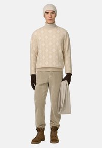 Beige stickad tröja med diamantmönster, bruna manchesteryxor, bruna handskar, bruna stövlar och matchande beige stickad mössa. Håller en ljusbeige scarf.