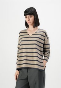 Beige og marineblå stripete genser med V-hals, lange ermer, avslappet passform og myk tekstur, kombinert med grå bukser.
