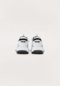 White sneakers with black accents, textured rubber soles, and a pull tab at the back. Features a lace-up design with visible stitching.