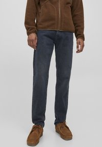 Jeans de mezclilla azul oscuro con corte recto, combinados con una chaqueta de polar marrón y zapatos marrones, con un ajuste relajado y tejido texturizado.