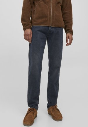 Jeans de mezclilla azul oscuro con corte recto, combinados con una chaqueta de polar marrón y zapatos marrones, con un ajuste relajado y tejido texturizado.