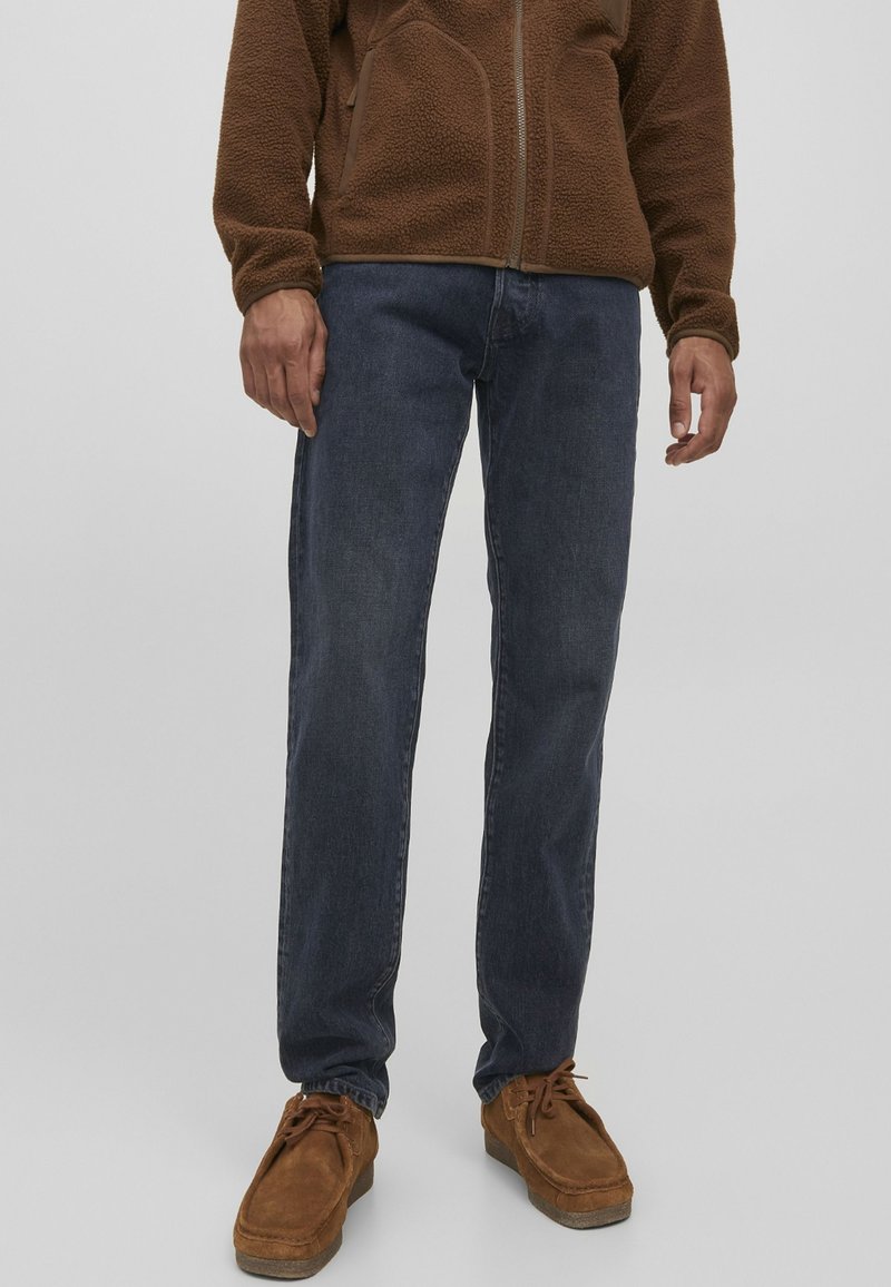 Jeans de mezclilla azul oscuro con corte recto, combinados con una chaqueta de polar marrón y zapatos marrones, con un ajuste relajado y tejido texturizado.