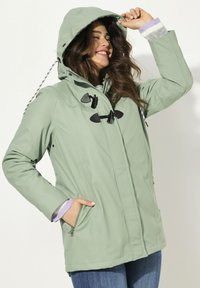Ljusgrön vattentät jacka med dragkedjefickor, svarta snoddar och huva. Har randiga manschetter och en slät textur.