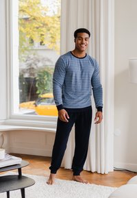 Ensemble de détente bleu marine comprenant un haut rayé à manches longues avec des poignets côtelés et un pantalon assorti. Tissu doux, coupe décontractée. Sol en bois et rideaux visibles.