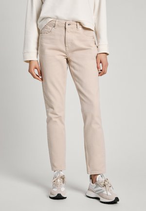 Jeans in cotone beige chiaro con taglio dritto, tasche frontali e zip, abbinati a sneaker grigie chiare e un felpa corta bianca.