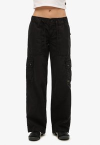 Schwarze Cargo-Hosen mit lockerer Passform, elastischem Bund, Kordelzugverschluss und mehreren seitlichen Taschen mit Knopfakzenten.