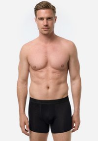 Boxer da uomo neri realizzati in materiale morbido con una cintura elastica che presenta un logo. Modello in piedi senza camicia, sfondo neutro.