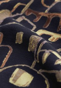 Gros plan sur un tissu foncé avec des motifs géométriques et animaliers tissés en beige et tons bruns.