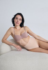 BH og høyhalsede truser i myk beige og lys rosa stoff, med glatte teksturer og et minimalistisk design.