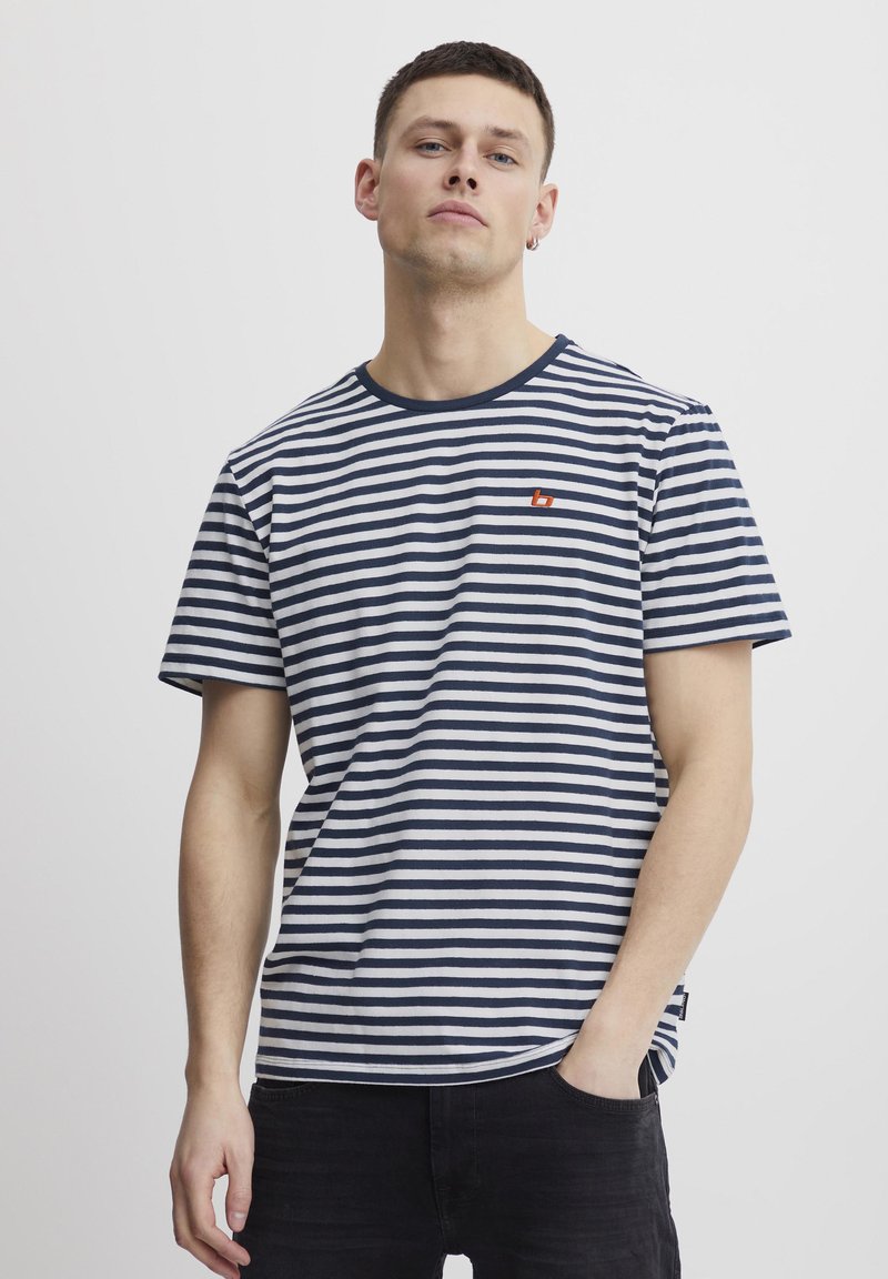Navy and white striped t-shirt in cotton fabric, crew neck with ribbed trim, featuring a small red logo on the chest. Short sleeves, relaxed fit.