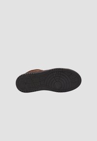 Brązowy zamszowy but z czarną gumową podeszwą o fakturze z okrągłymi i liniowymi wzorami dla lepszej przyczepności.