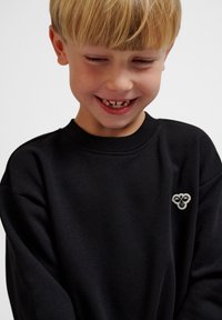 Svart sweatshirt gjord av bomull med ribbad rund hals och broderad design på bröstet. Slät textur, avslappnad passform.