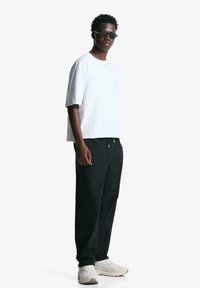 Tricou alb cu mânecă scurtă, croială relaxată, asortat cu pantaloni negri largi. Accesorizat cu ochelari de soare închiși la culoare și adidași albi. Design simplu.