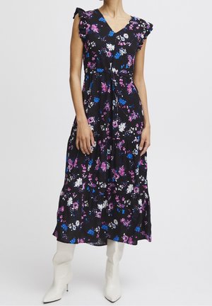 Mujer con vestido midi negro con flores rosas, azules y blancas, mangas con volantes y botas blancas de tacón alto.