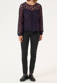 Haut en dentelle marine à manches longues avec motifs floraux et encolure festonnée, associé à un pantalon noir slim et des mocassins noirs massifs.