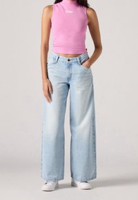 Jasnoniebieskie spodnie dżinsowe typu wide-leg, wykonane z denimu, o luźnym kroju. Połączone z różową bluzką bez rękawów z białym logo oraz białymi trampkami.